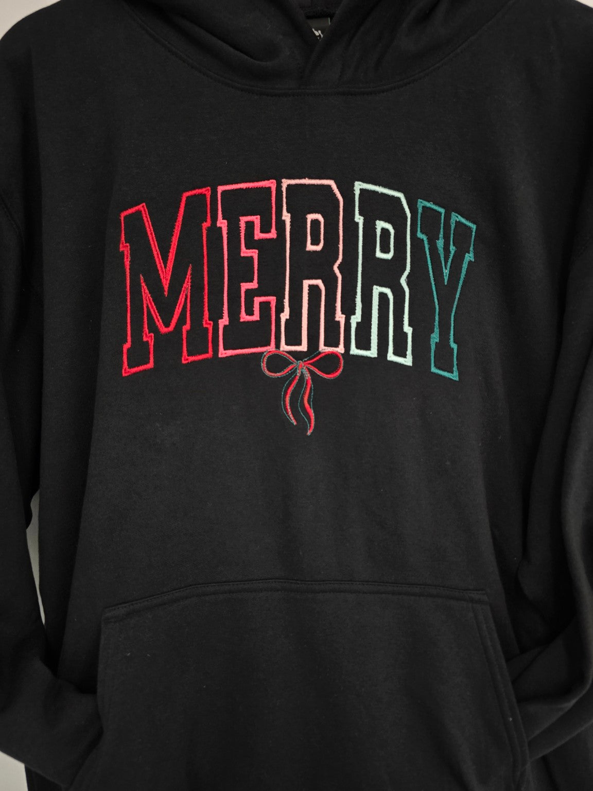 Close-up of colourful varsity Merry embroidery and bow