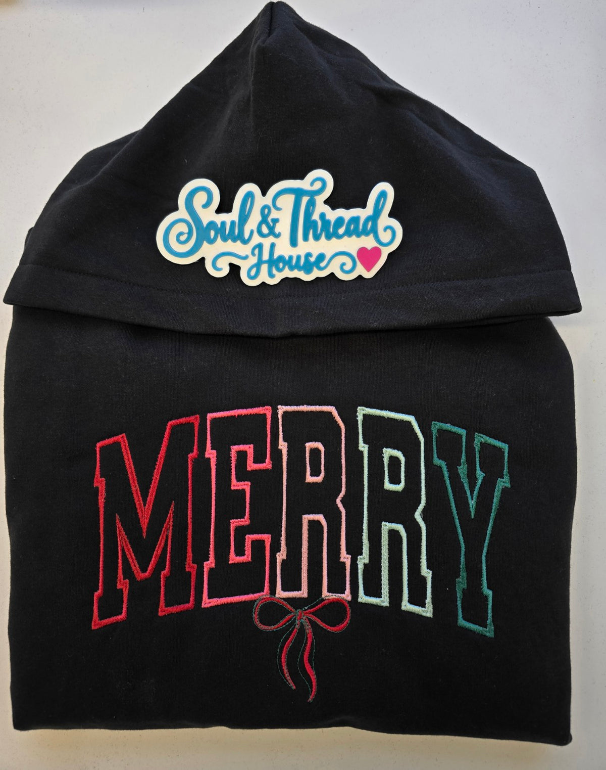 Folded black Merry Christmas hoodie showing embroidered lettering
